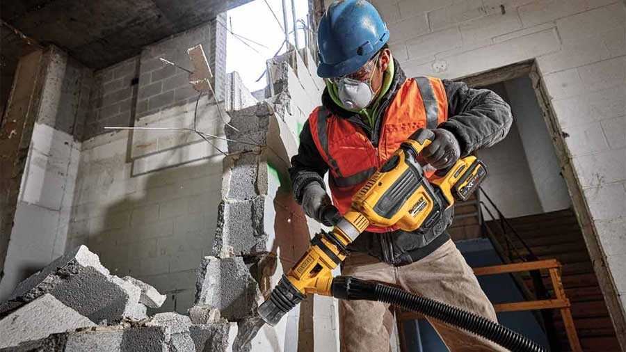 Ouvrier avec un casque et un masque casse un mur de brique avec un perforateur dewalt puissant