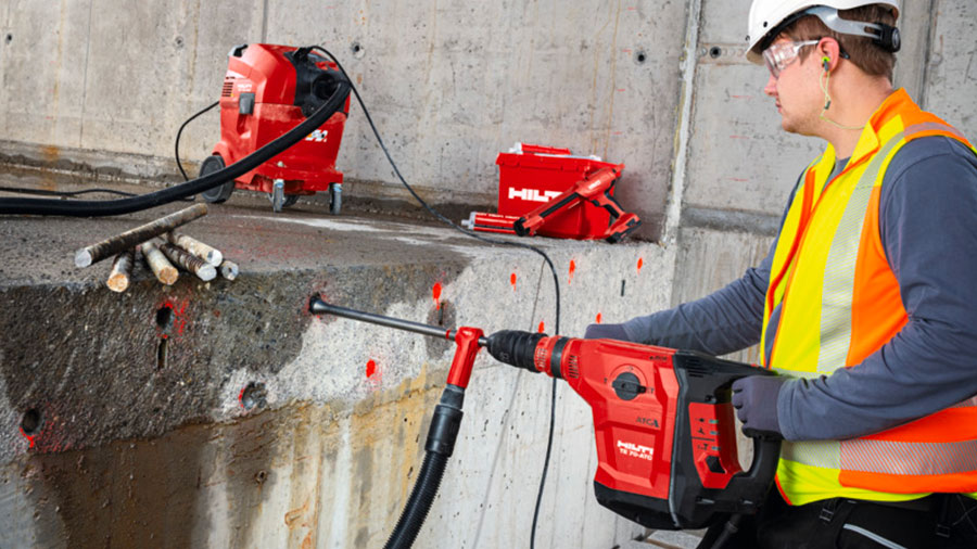 Homme-avec-un-casque-sur-un-chantier-qui-perce-un-mur-de-pierre-avec-un-perforateur-burineur