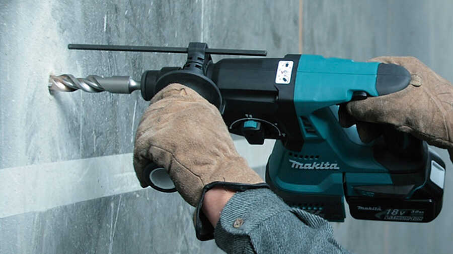 Main protégée par gant en cuir manipule un perforateur burineur pour percer un mur de béton